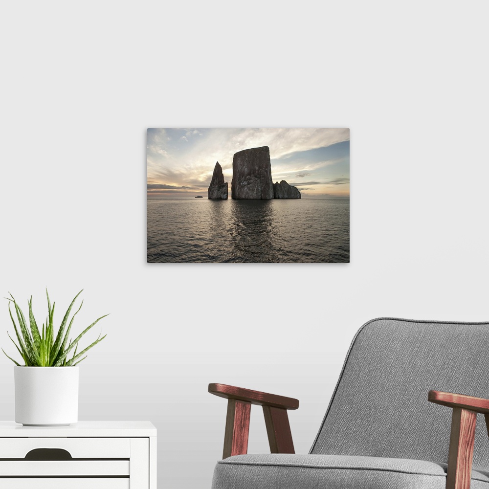 A modern room featuring An expedition vessel passes near a large rock formation at sunset. Pacific Ocean, Galapagos Islan...