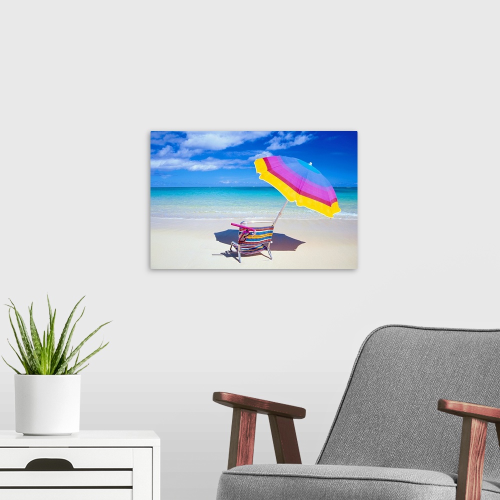 A modern room featuring A large photograph of a colorful beach chair and umbrella sitting solely on the sand close to the...