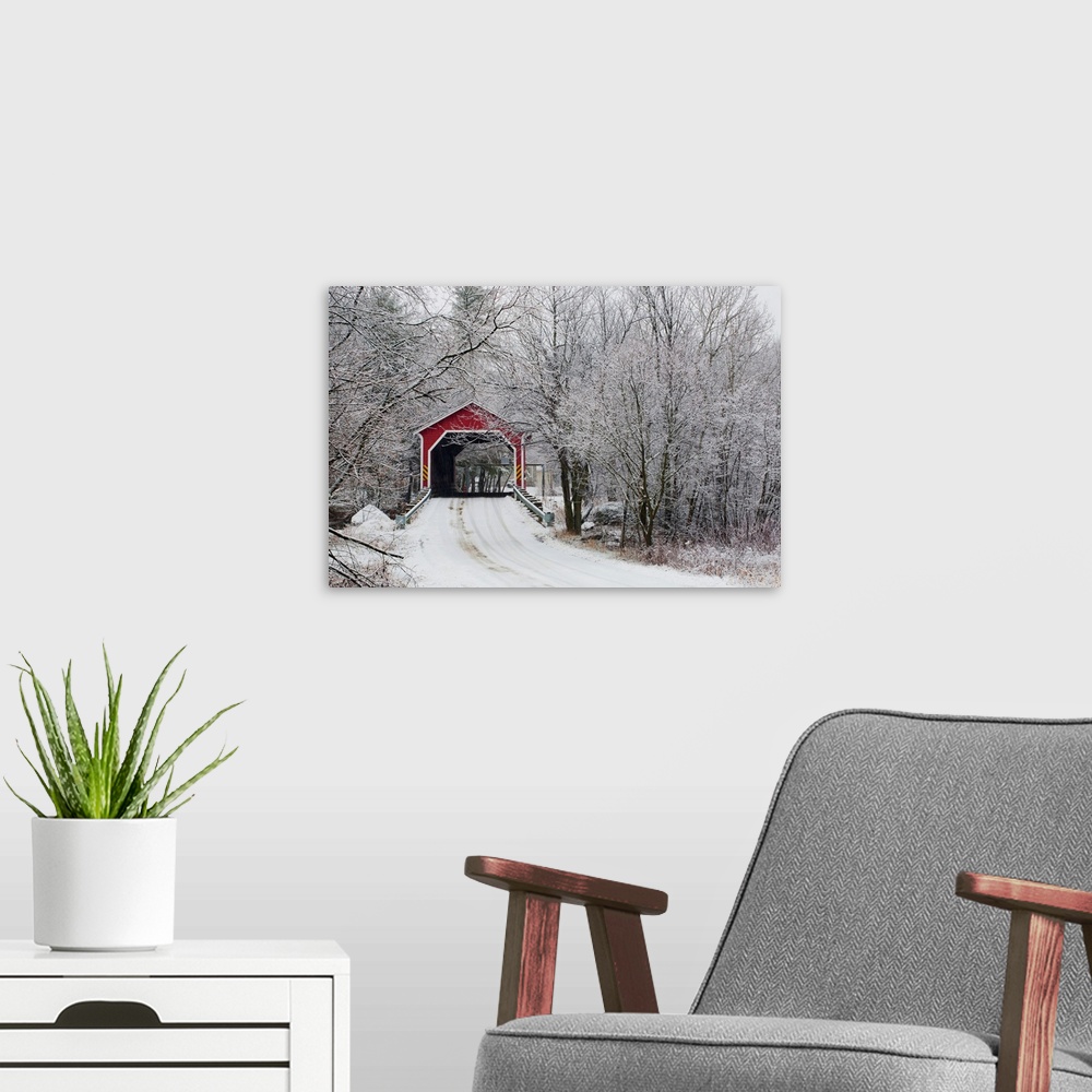 A modern room featuring Snow covered trees surround a road that leads up to a covered bridge.