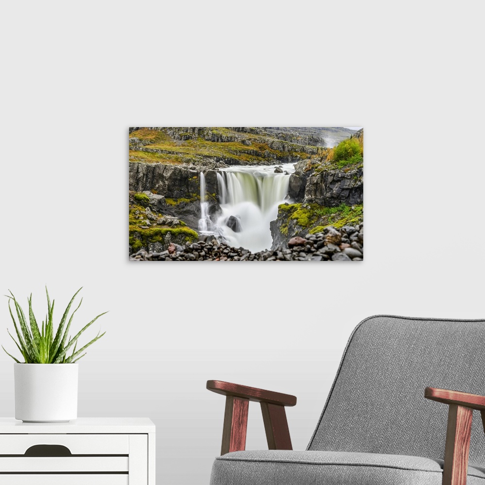 A modern room featuring A waterfall over a rocky landscape in autumn colours; Djupivogur, Eastern Region, Iceland.
