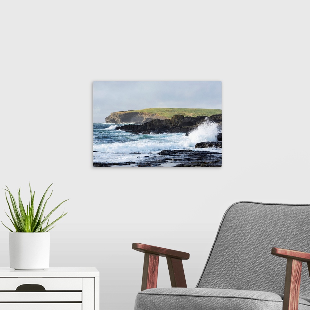 A modern room featuring Waves crashing into rocky coast with large grassy hill and cliffs in background, Kilkee, County C...