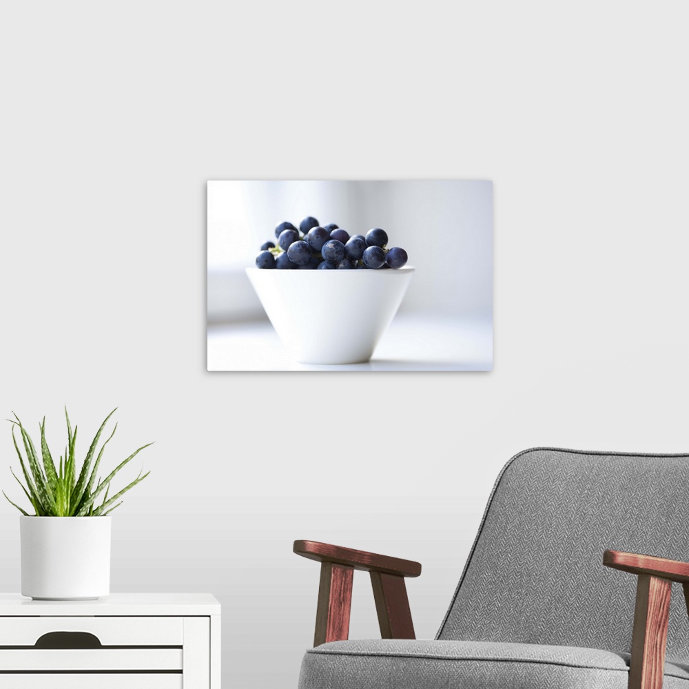 A modern room featuring Grapes in small white bowl on window sill.