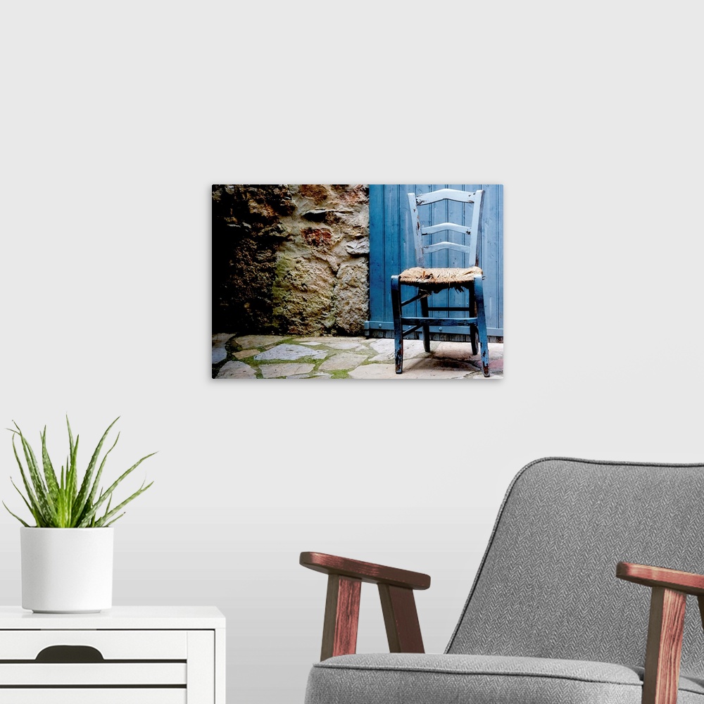 A modern room featuring Front capture of old blue wooden chair with damaged caned seat, at doorstep of house with blue wo...