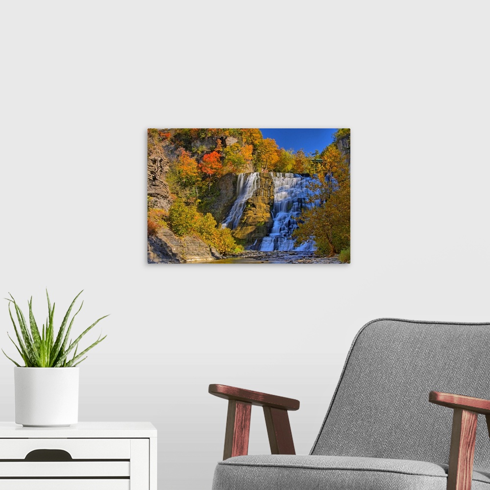 A modern room featuring This large piece is of a sizeable waterfall that is surrounded by autumn colored trees and foliage.