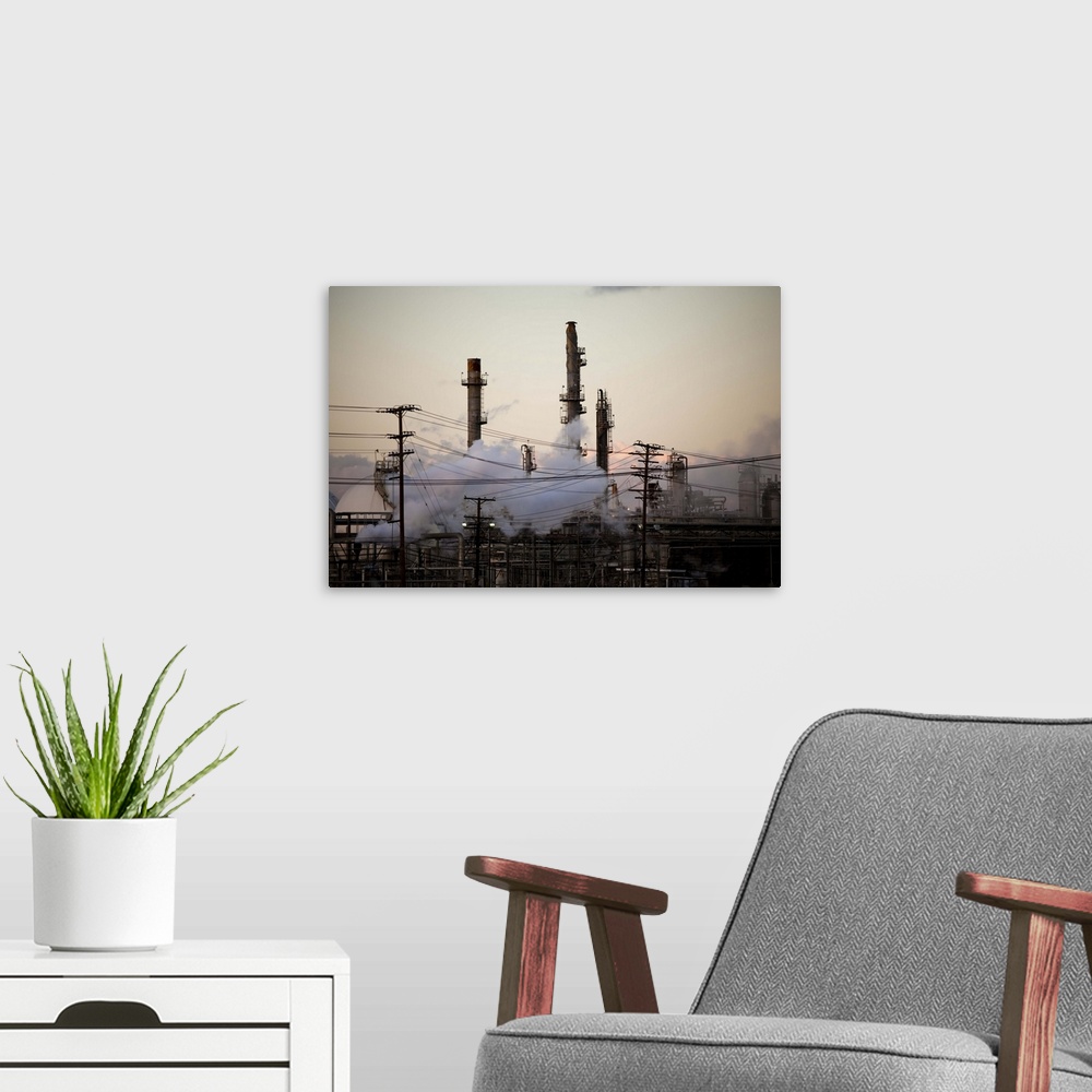 A modern room featuring Smoke stacks and distillation towers rise out of a thicket of power lines and plumes of steam at ...