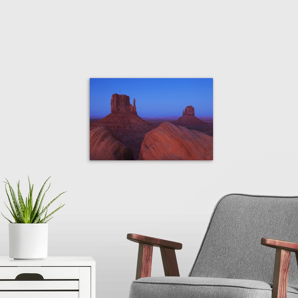 A modern room featuring Monument Valley at dusk, with view of the West Mitten, the East Mitten and some foreground rock f...