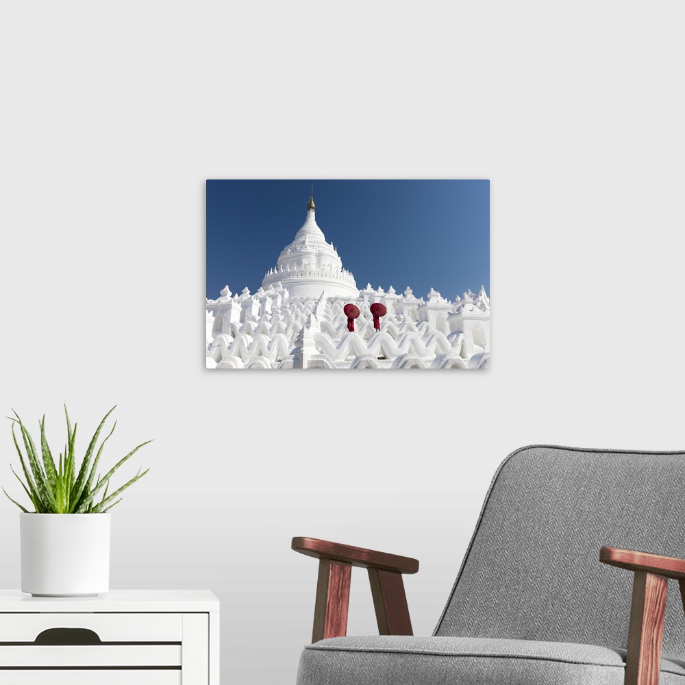 A modern room featuring Two young Buddhist monks stand on the white walls of Hsinbyume Pagoda holding red umbrellas, Ming...