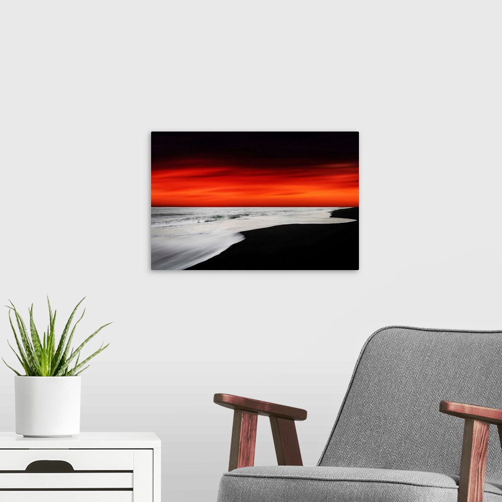 A modern room featuring A dramatic photograph of a blazing sky hanging over a white seascape seen from a black sand beach.