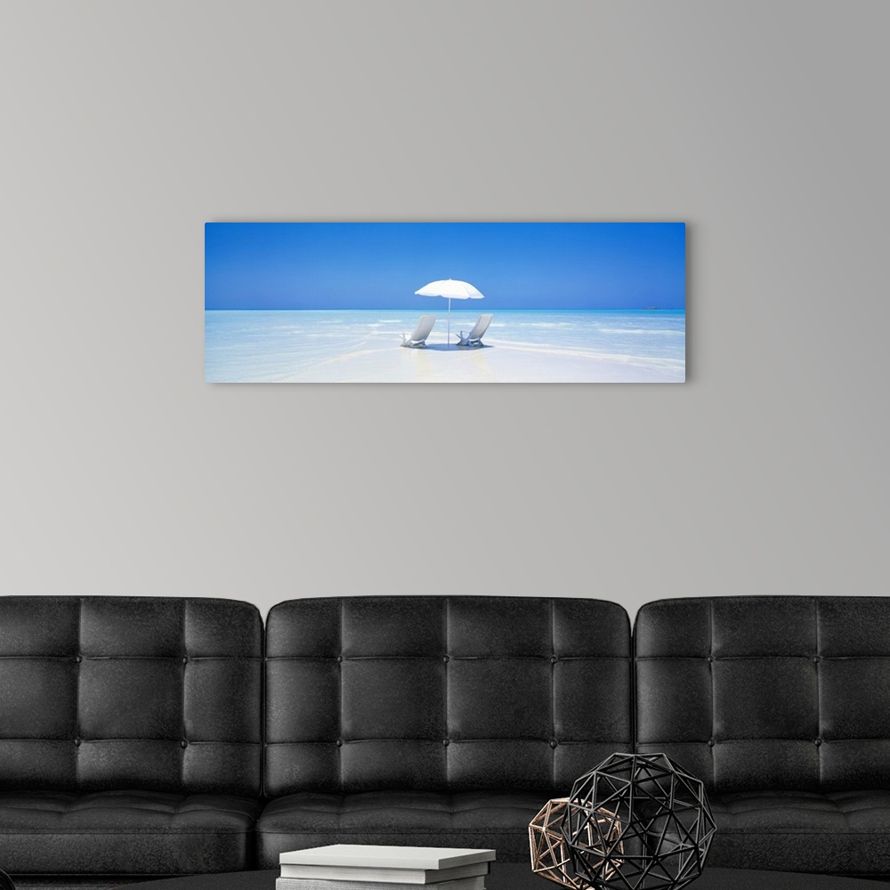 A modern room featuring A panoramic photograph displaying two chairs sitting underneath an umbrella on a sandy beach in M...
