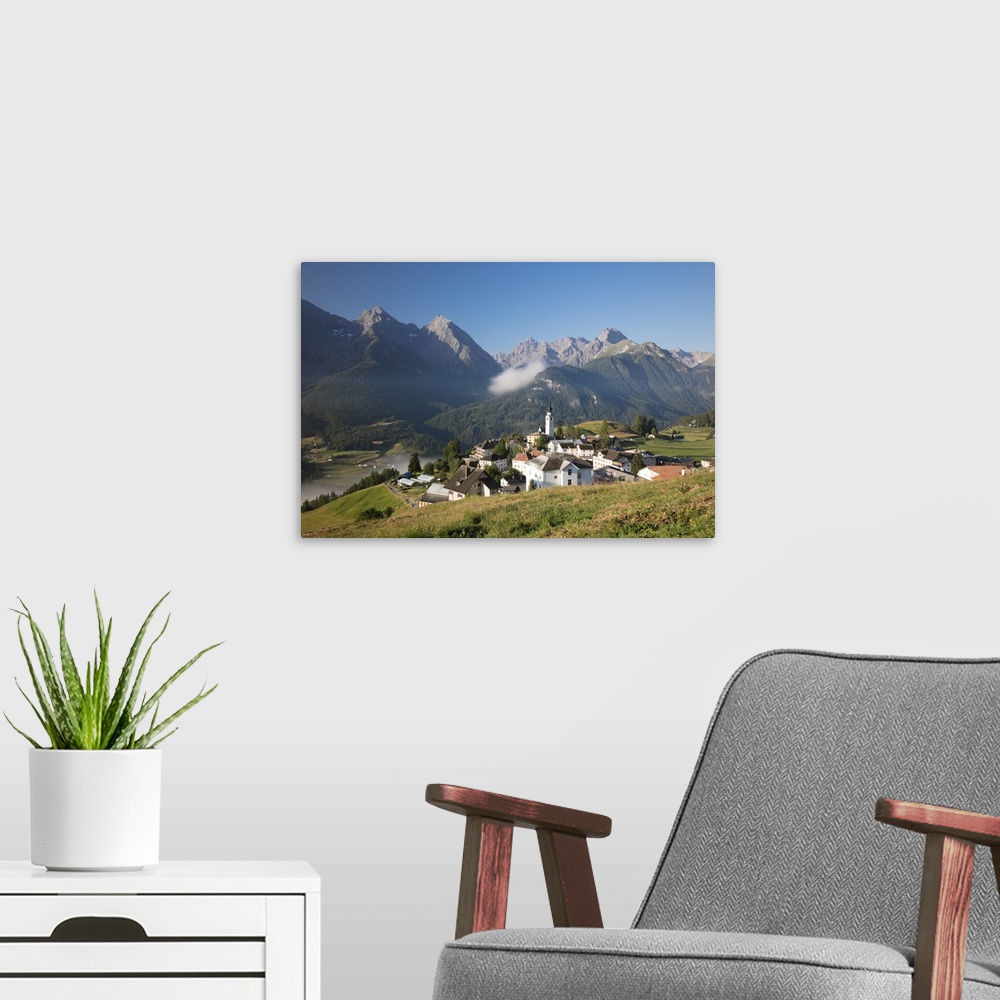 A modern room featuring Green meadows frame the the alpine village of Ftan, Inn district, Canton of Graubunden, Engadine,...