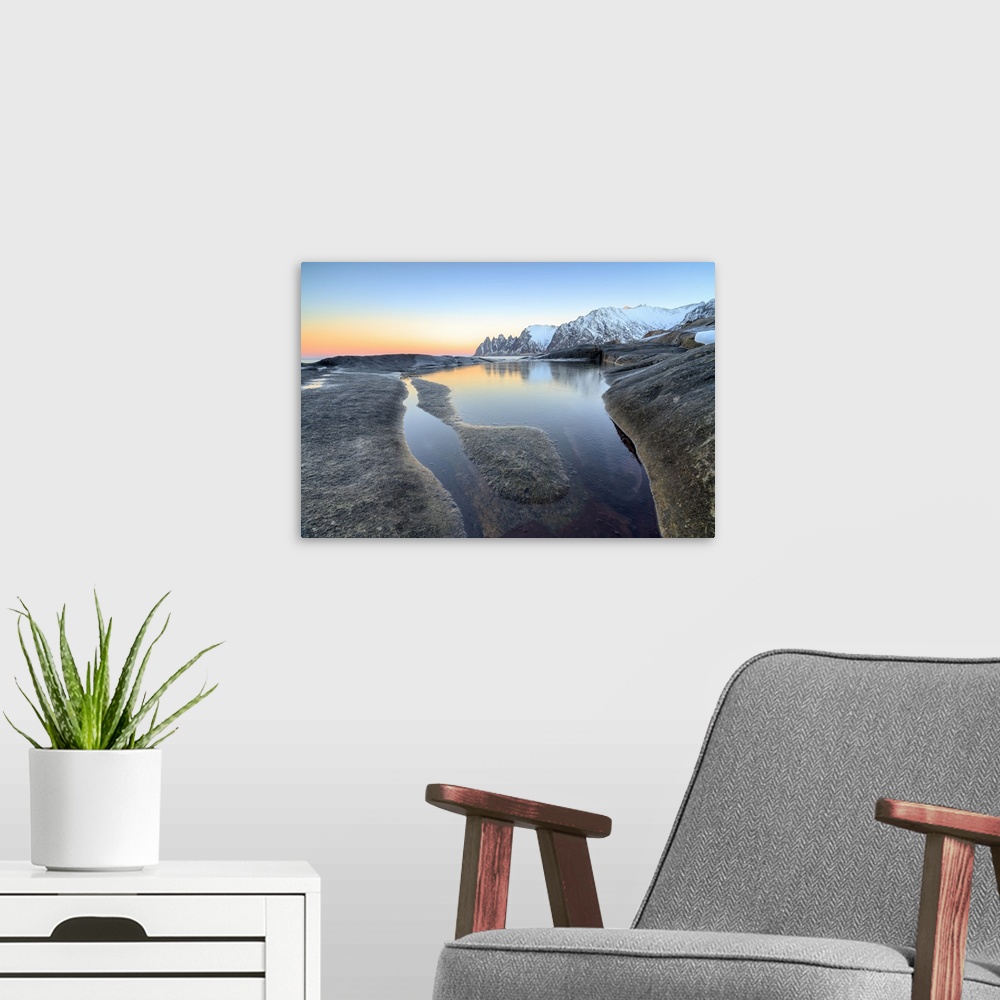 A modern room featuring Orange sky at sunset reflected on snowy peaks and the frozen sea surrounded by rocks Tungeneset, ...