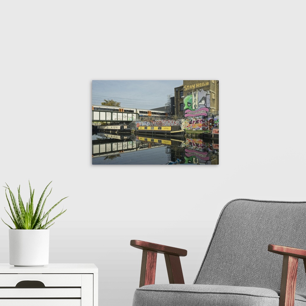 A modern room featuring Overground train drives past canal by artists studios and warehouses in Hackney Wick, London, Eng...