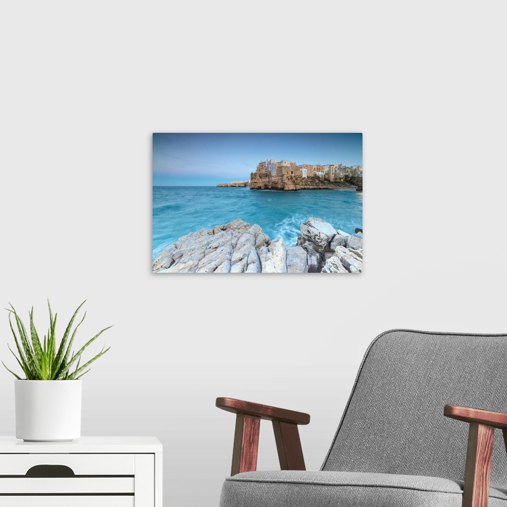A modern room featuring Turquoise sea at dusk framed by the old town perched on the rocks, Polignano a Mare, Province of ...