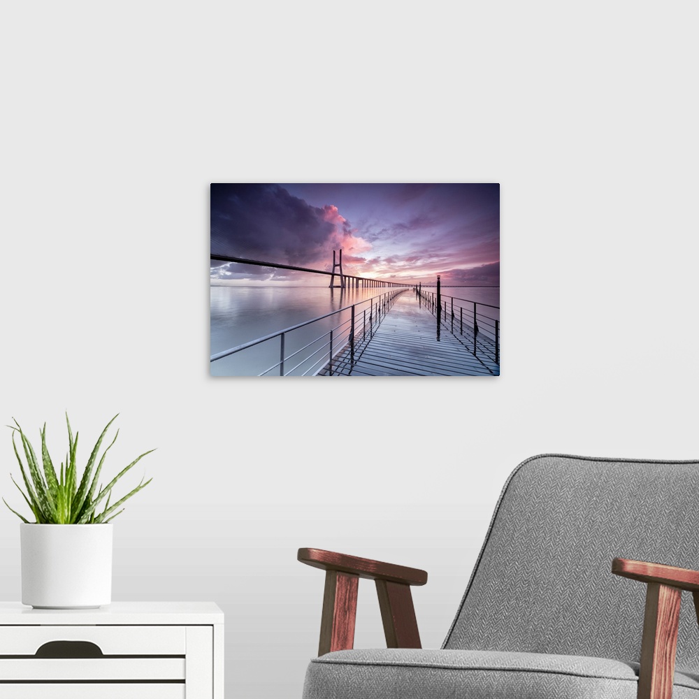 A modern room featuring Sunrise colors the clouds reflected in Tagus River and frame the Vasco da Gama bridge in Lisbon, ...