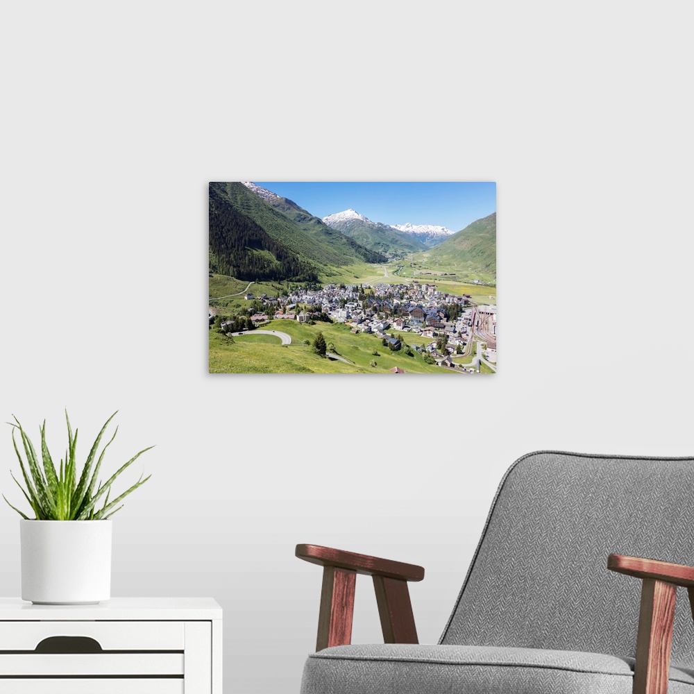 A modern room featuring The alpine village of Andermatt surrounded by green meadows, and snowy peaks in the background, C...