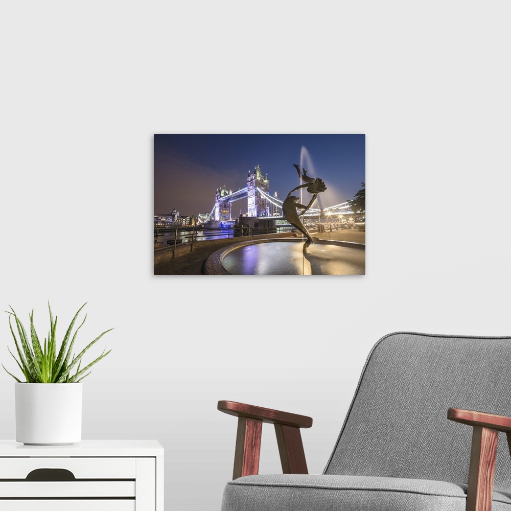 A modern room featuring The Girl With A Dolphin Fountain frames Tower Bridge reflected in the River Thames at night, Lond...