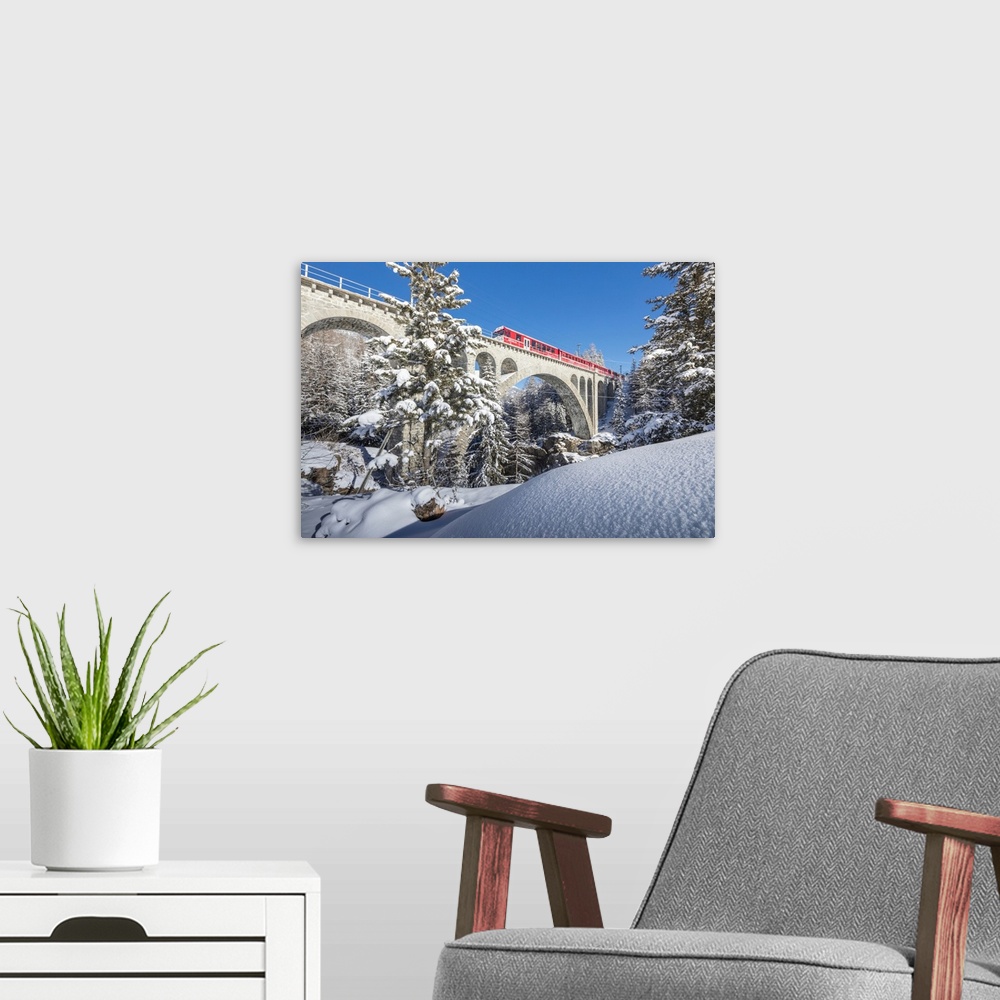 A modern room featuring The red train on viaduct surrounded by snowy woods, Cinuos-Chel, Canton of Graubunden, Engadine, ...