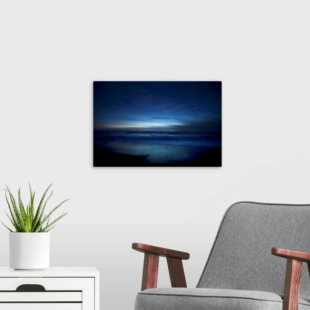 A modern room featuring Landscape, oversized photograph of deep blue ocean waters along the beach, surrounded by the dark...