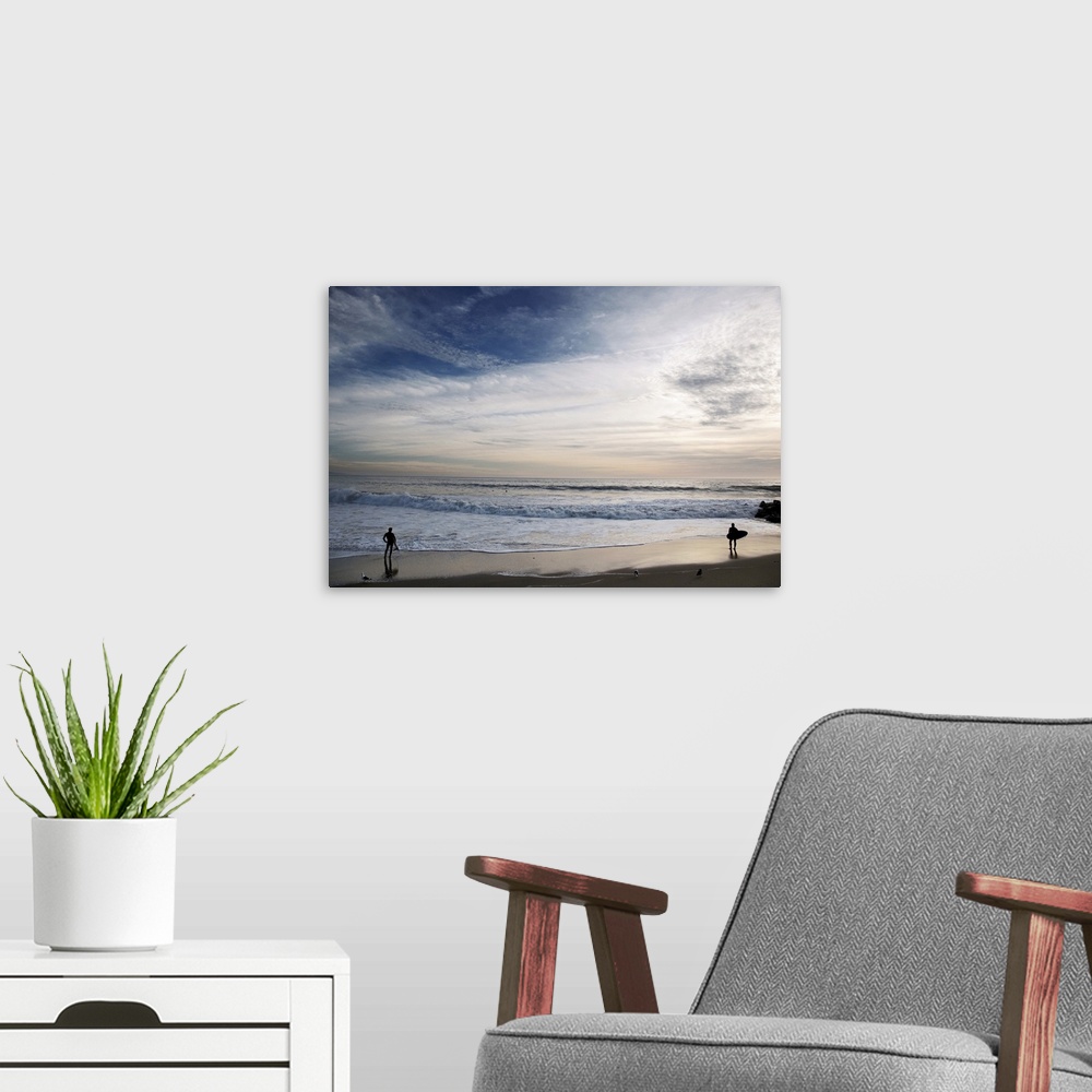 A modern room featuring Huge photograph displays a couple individuals with surfboards standing on the edge of the ocean a...