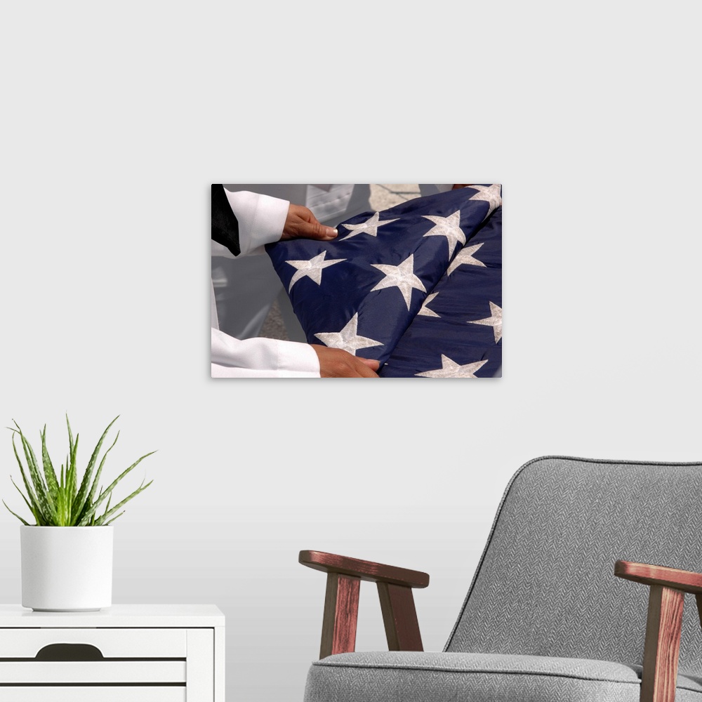 A modern room featuring Sailors assigned to the colors detail fold the national ensign.