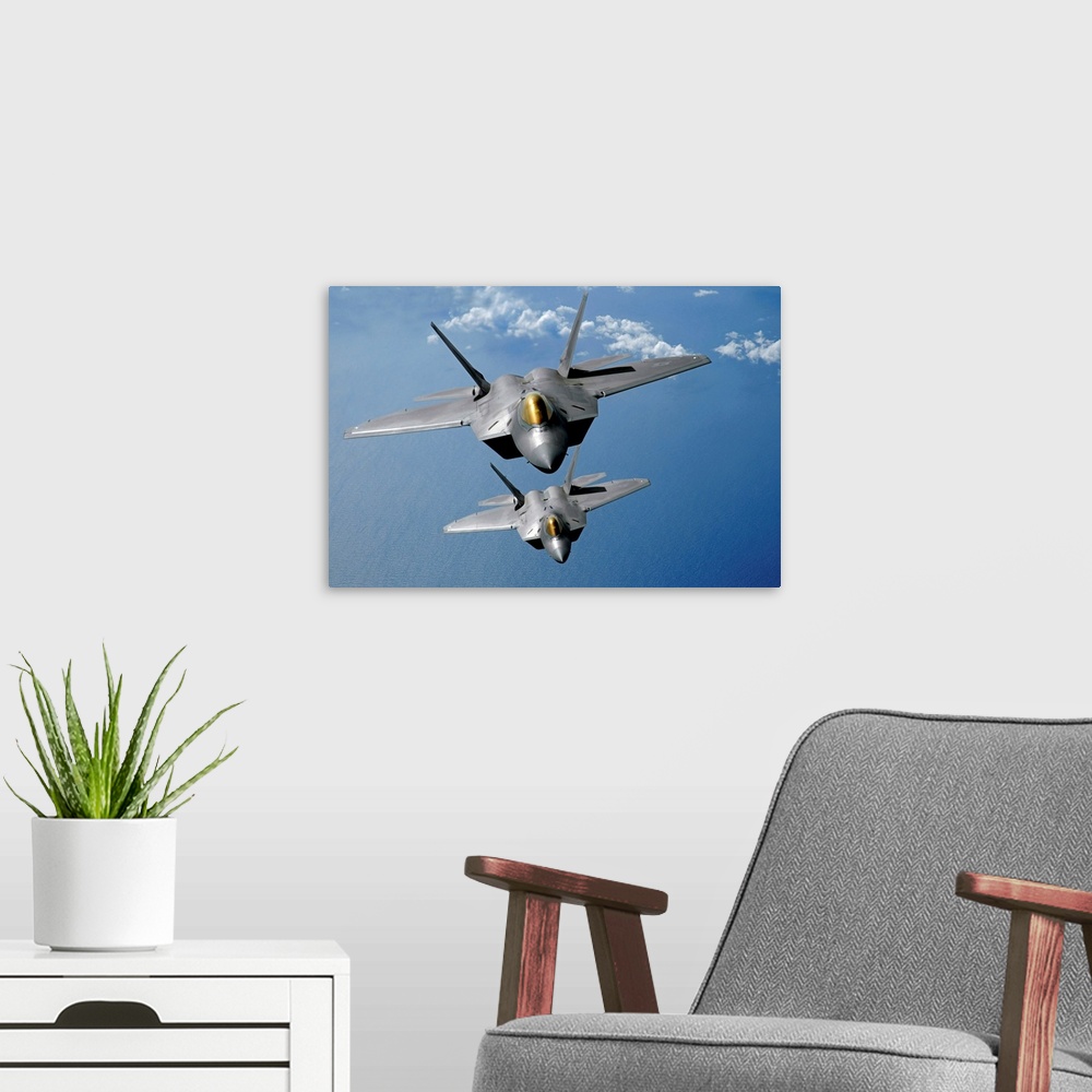 A modern room featuring Large, landscape photograph of two F22 Raptors flying high in the sky above the blue waters of th...