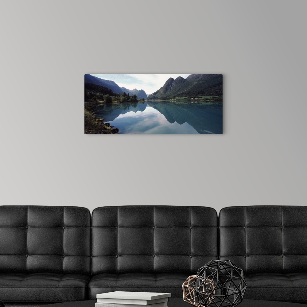 A modern room featuring A large piece that is a photograph of mountains lining a body of water that reflect in the still ...