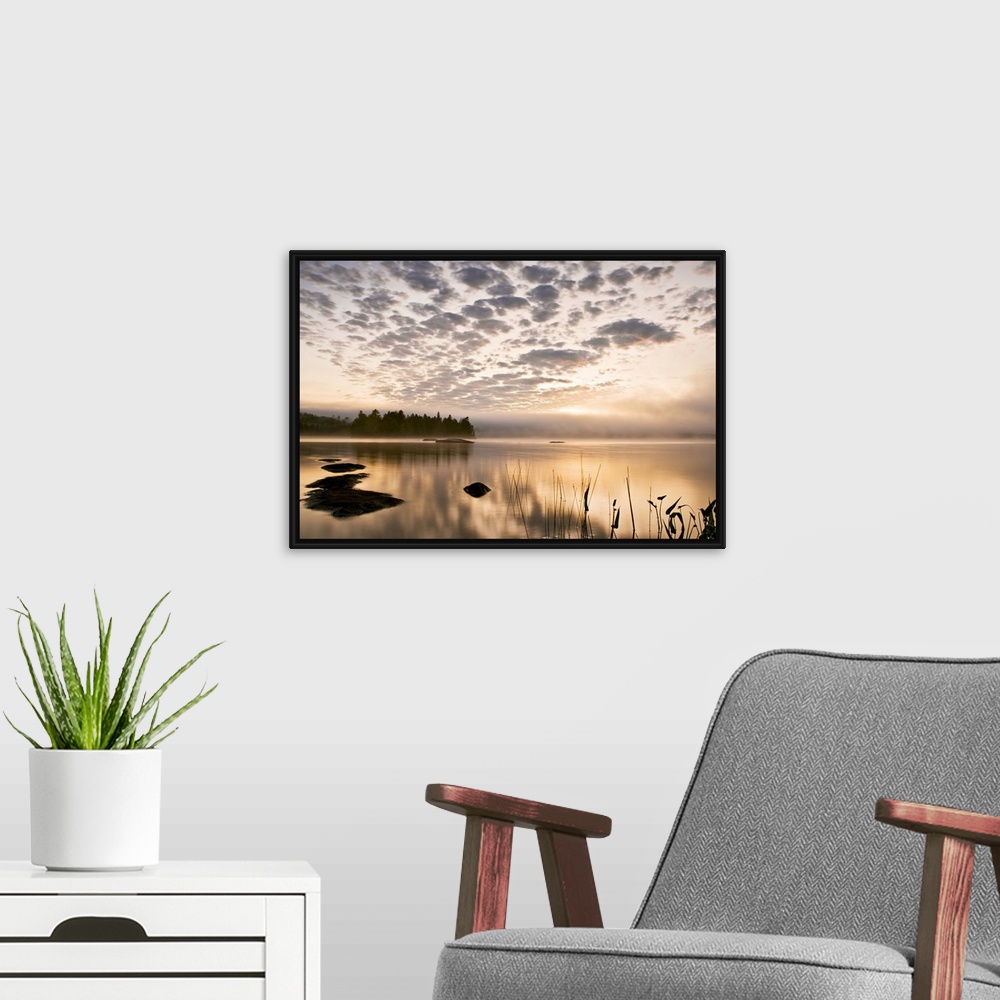 A modern room featuring Horizontal photograph on a big wall hanging of the sun set reflecting in a large body of water, a...