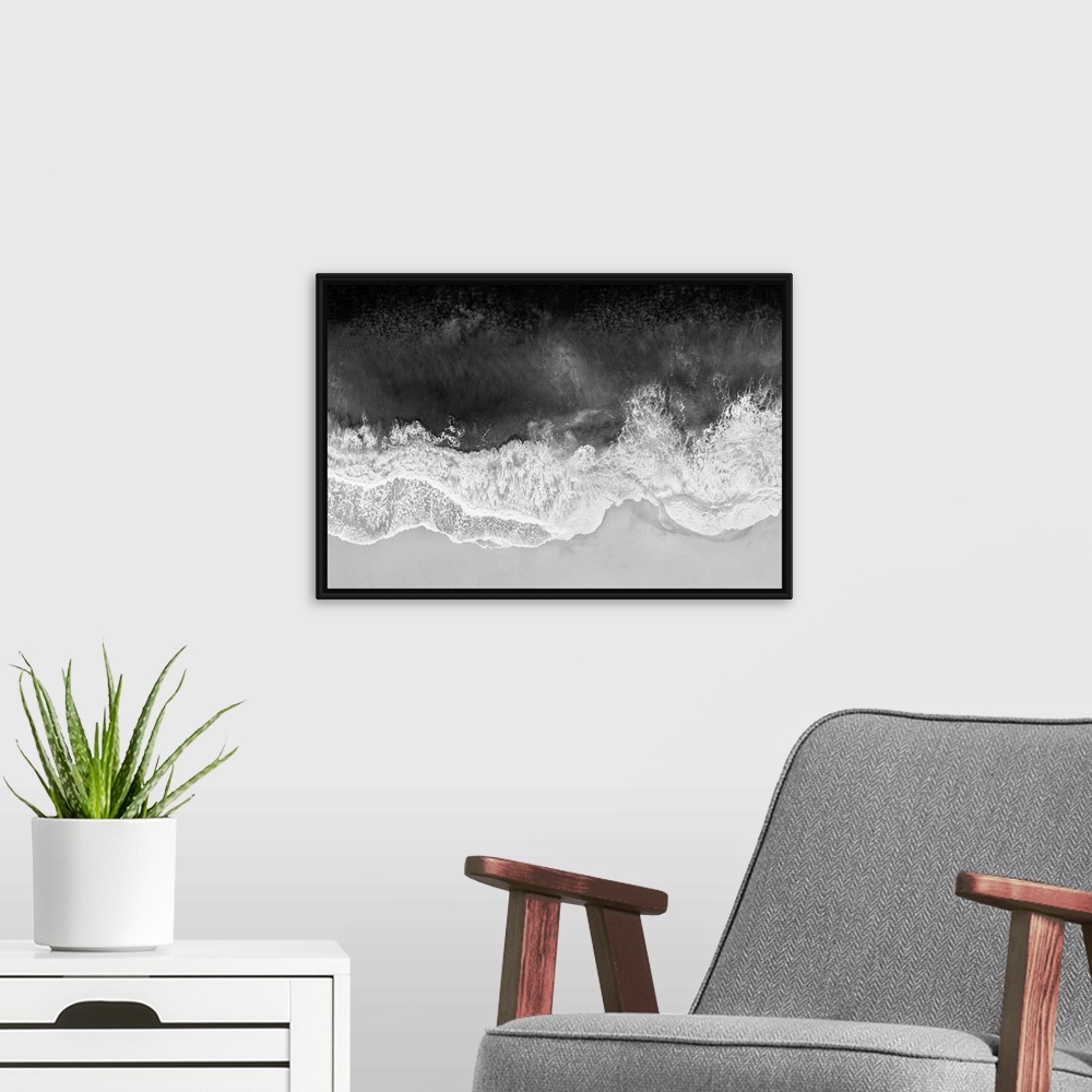 A modern room featuring One artwork in a series of aerial shots of a beach as dark gray waves break upon the shore.