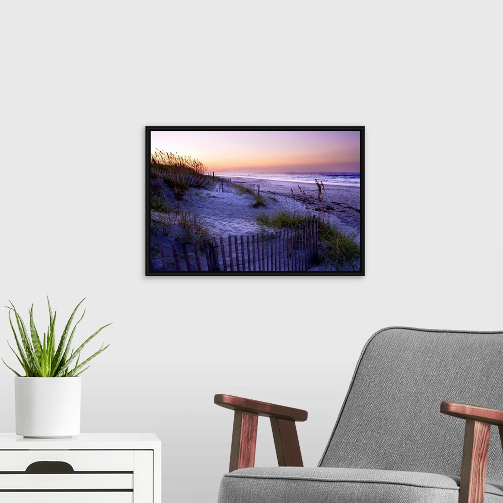 A modern room featuring A landscape photograph of a dune covered in sea grass and fences fills the foreground of this bea...