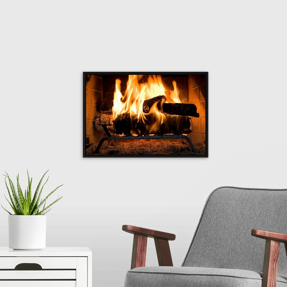 A modern room featuring A horizontal photograph of logs burning inside a personal, home fireplace lined with bricks