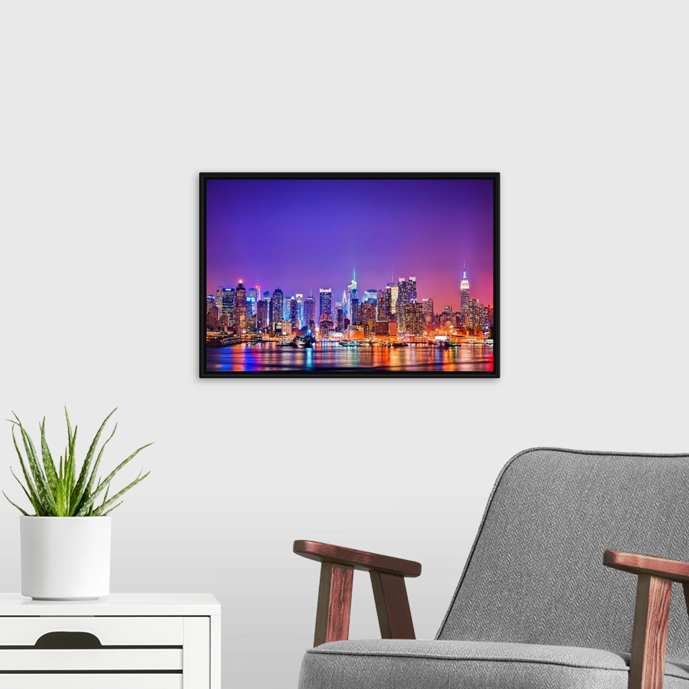 A modern room featuring Photograph of New York skyline at night with the Hudson River in foreground.  The building lights...