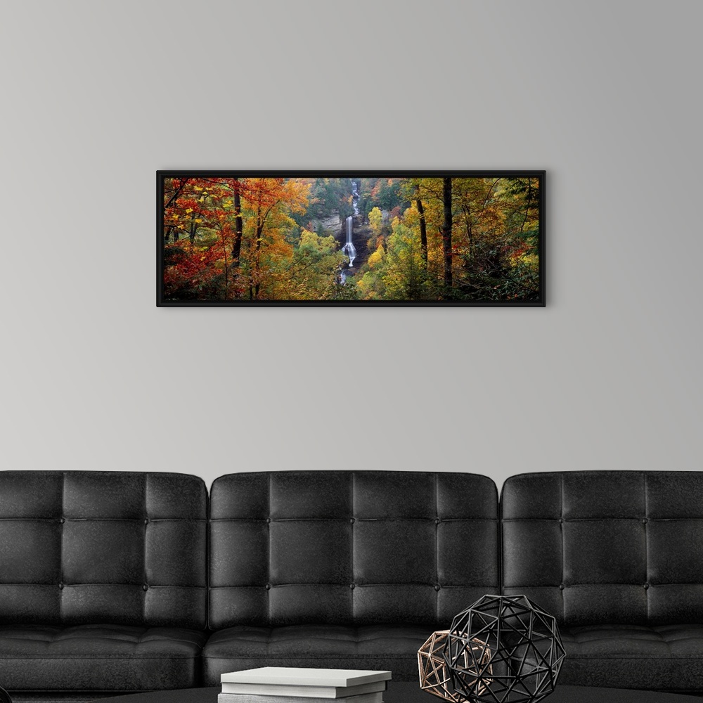 A modern room featuring This panoramic wall art is a photograph of a waterfall cascading down a sheet rock face in an aut...