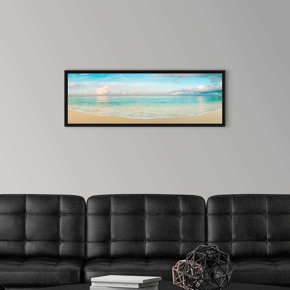 A modern room featuring A wide angle panoramic wall hanging of a calm tropical ocean, waves on the beach, and cumulus clo...