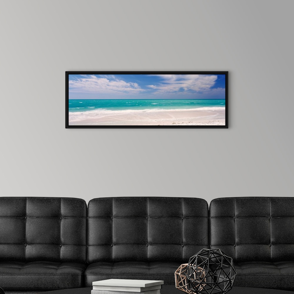 A modern room featuring Panoramic photograph of calm ocean with surf and sand in the foreground and cloudy sky above.
