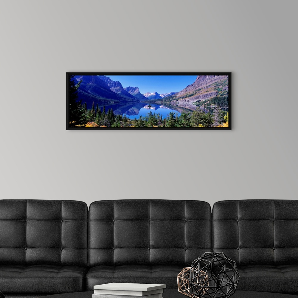 A modern room featuring A photographic print of rugged mountains with snow in the distance reflected in a crystal clear l...