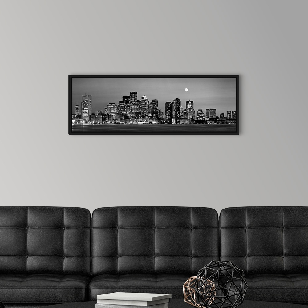 A modern room featuring A panoramic of the skyscrapers in Boston lit up at night and the moon above the city.