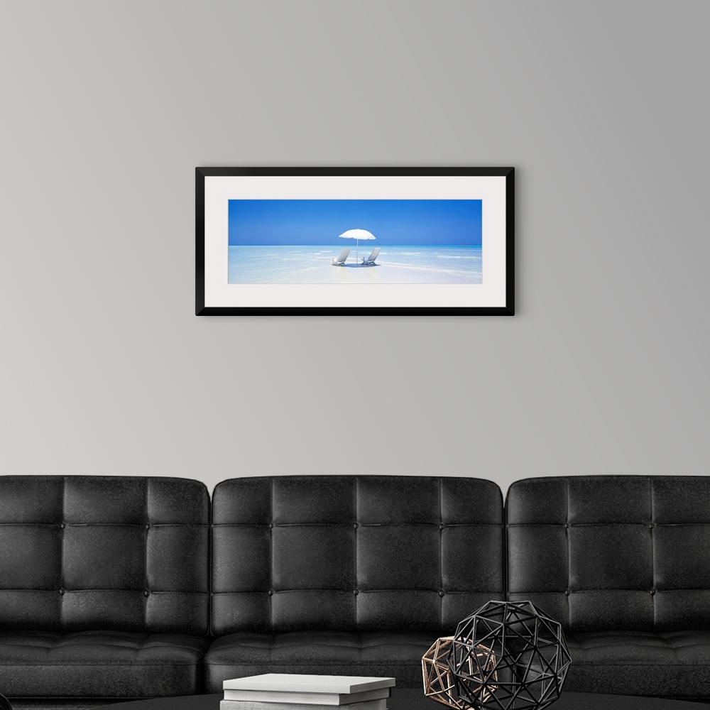 A modern room featuring A panoramic photograph displaying two chairs sitting underneath an umbrella on a sandy beach in M...