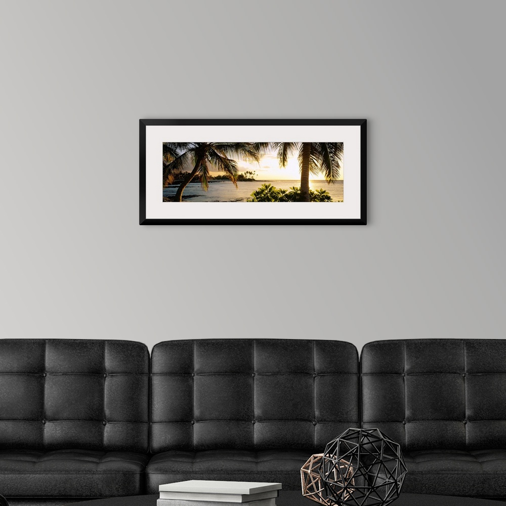 A modern room featuring Panoramic wall art photo for the office or home of the Hawaiian coast; palm trees frame the sun s...