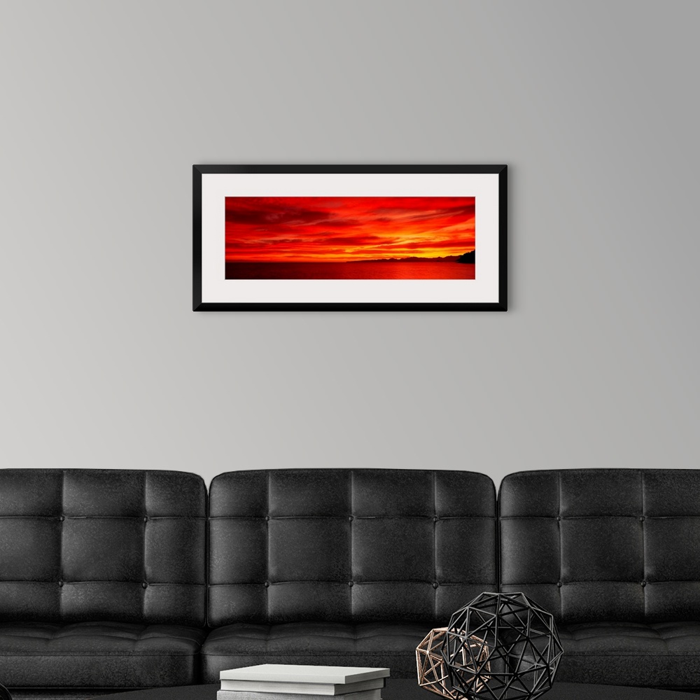 A modern room featuring Large wall image of a deep warm sunset over the ocean with a little strip of land on the right si...