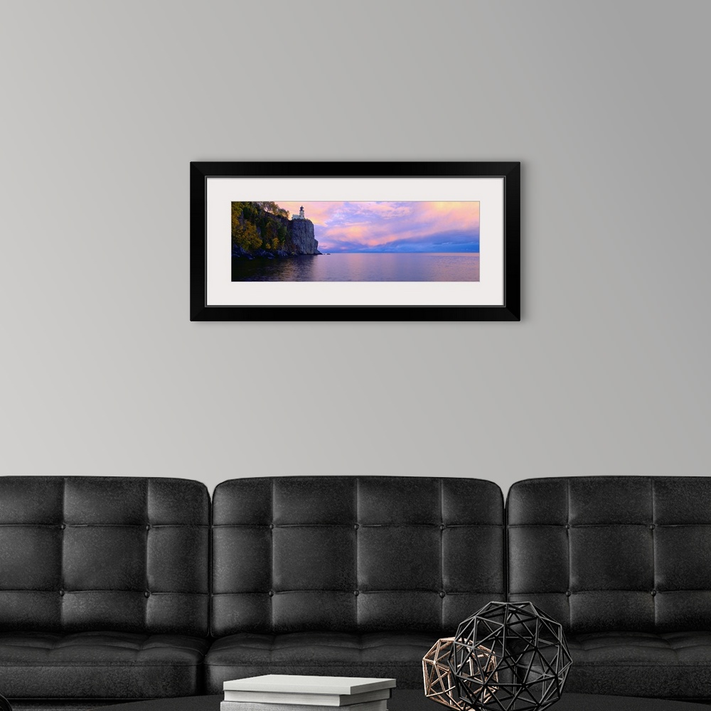 A modern room featuring Panoramic photo print of a lighthouse on top of a cliff overlooking the water at sunset.
