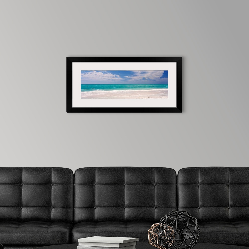 A modern room featuring Panoramic photograph of calm ocean with surf and sand in the foreground and cloudy sky above.