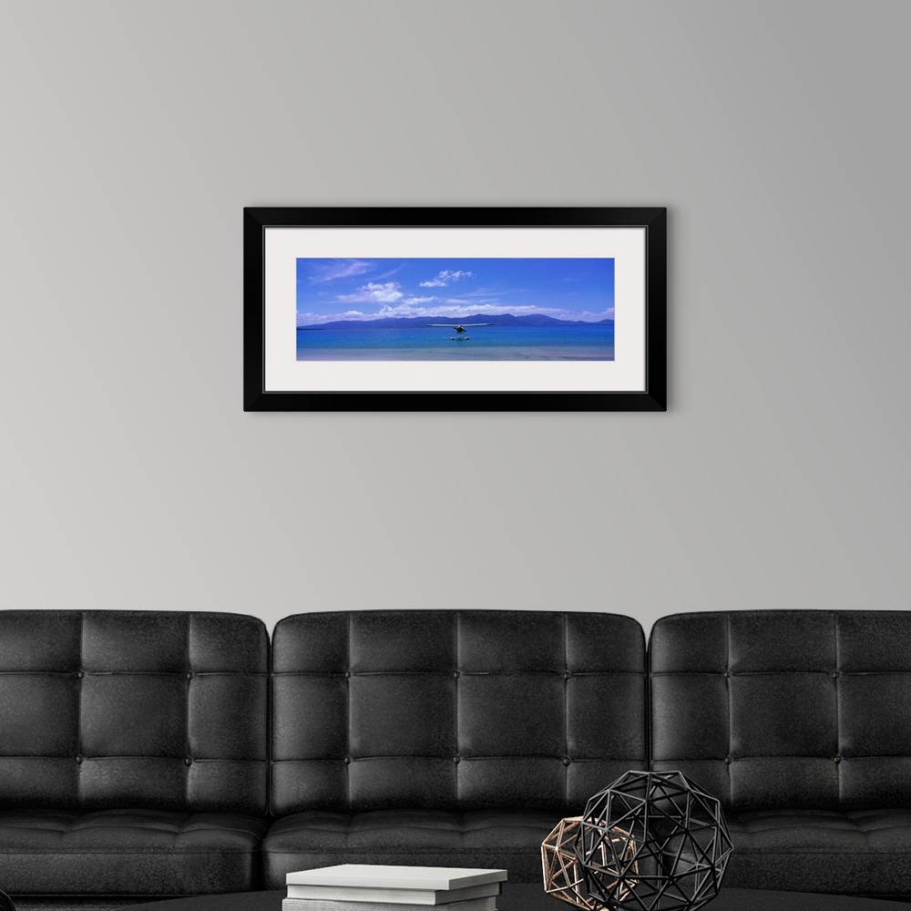 A modern room featuring Private propeller plane floating on the water near the shoreline with low mountains and cloudy sk...