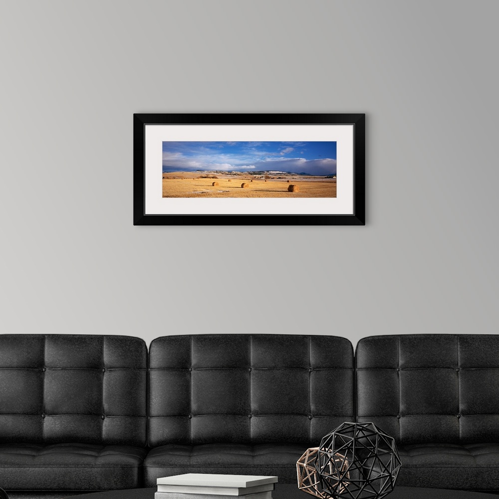 A modern room featuring Landscape photograph on a giant wall hanging of a vast, golden filed with hay bales, beneath a br...