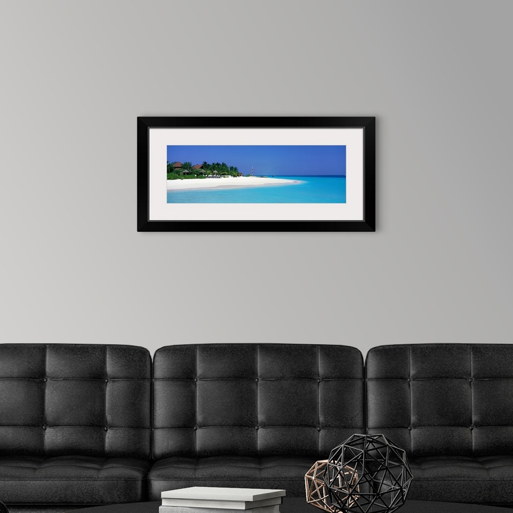 A modern room featuring This panoramic photograph is of a beach in Maldives with huts pushed back and surrounded by trees...