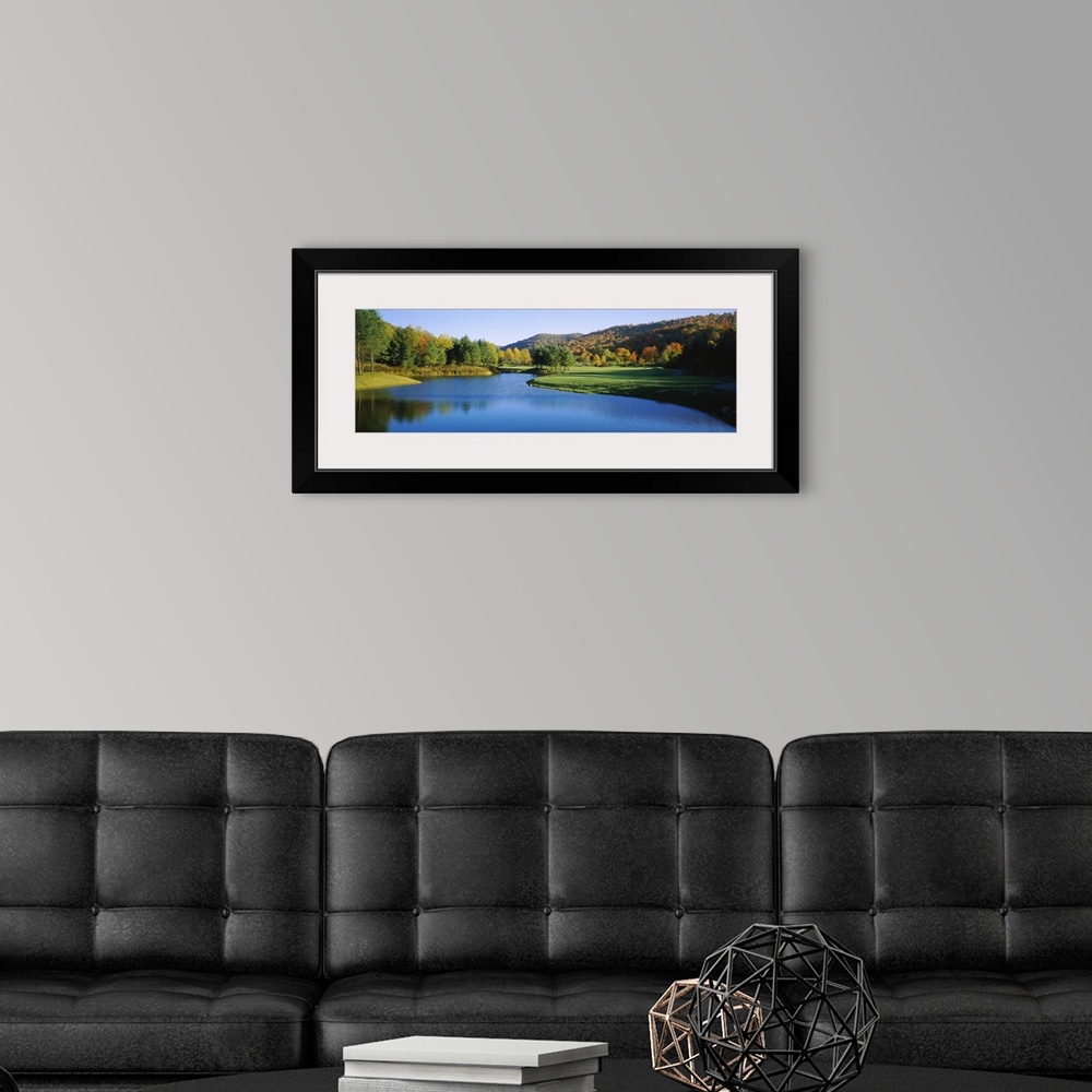 A modern room featuring Long horizontal canvas print of a golf course with a lake in the middle and fall foliage on rolli...