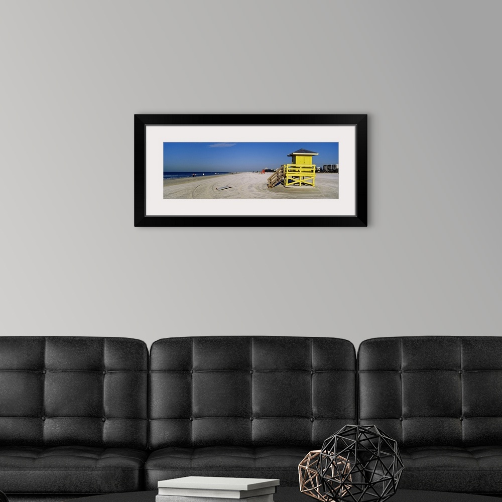 A modern room featuring A panoramic photograph of a mostly empty beach, there is a small shelter and abandoned surfboard ...