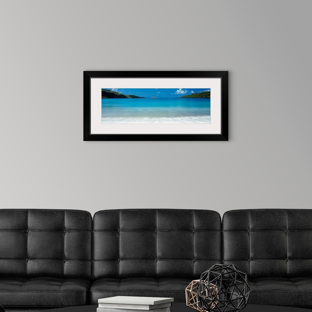 A modern room featuring Panoramic photograph of clear water in a calm sea washing up a tropical beach.