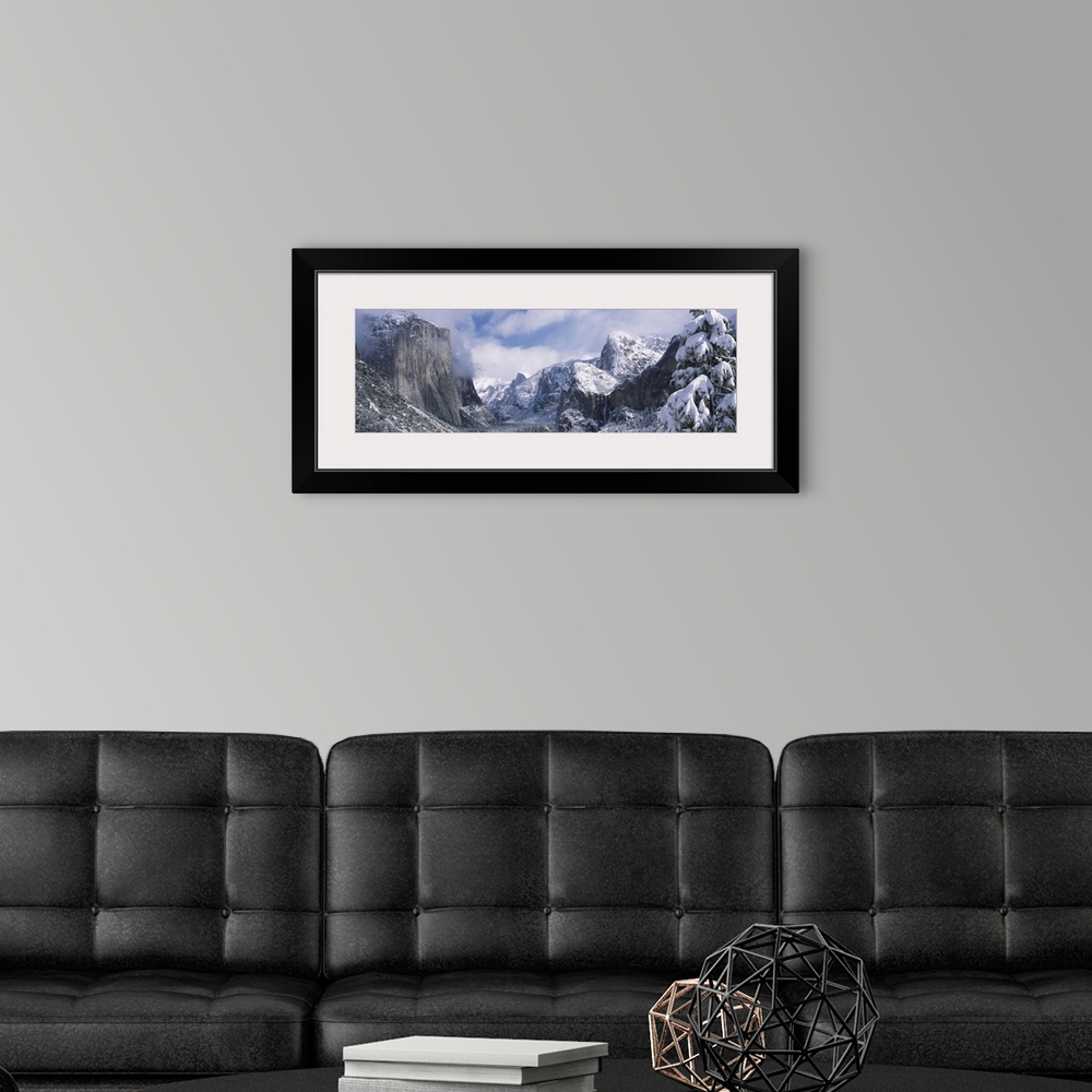A modern room featuring This panoramic photograph is taken of immense mountains that reach up into the clouds and are cov...