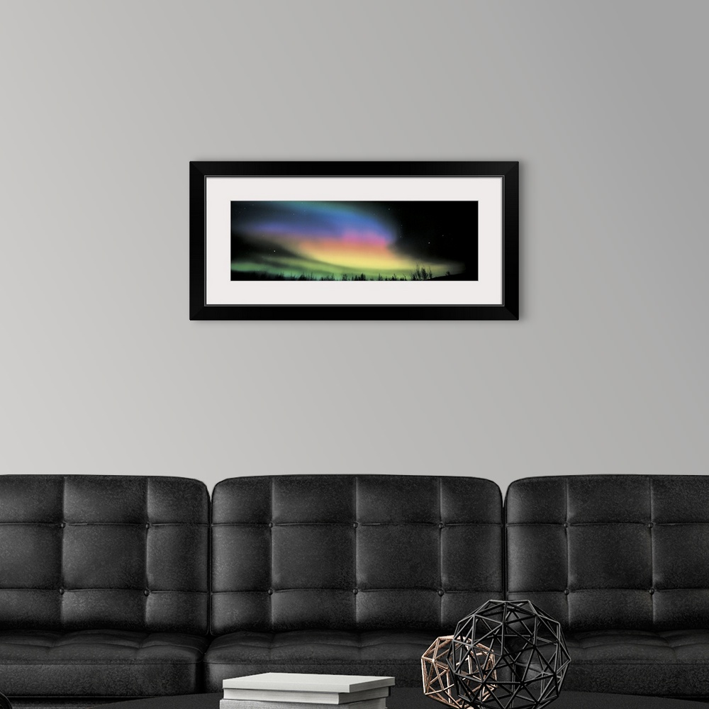 A modern room featuring Panoramic photograph taken of the northern lights. Swirls of color brighten the dark night sky.