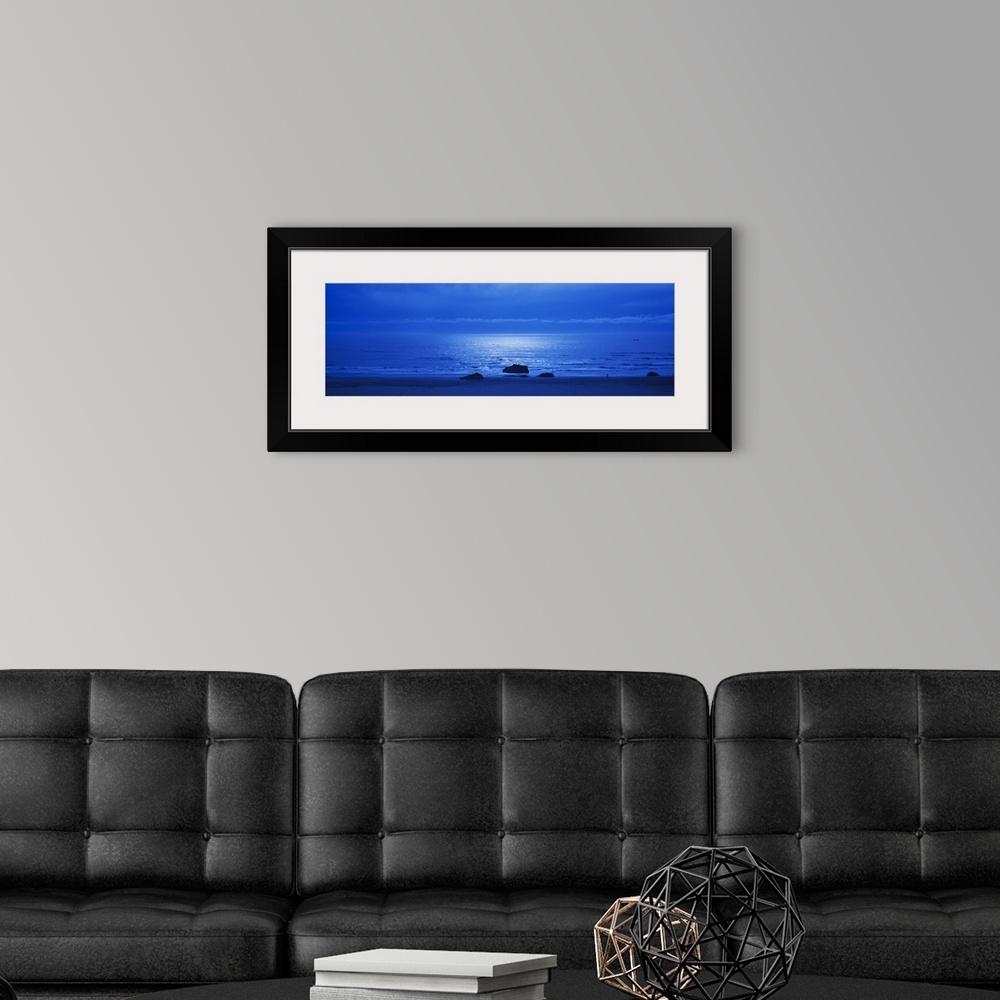 A modern room featuring Panoramic photograph of a monotone seascape with the moonlight reflecting off the waves, three so...